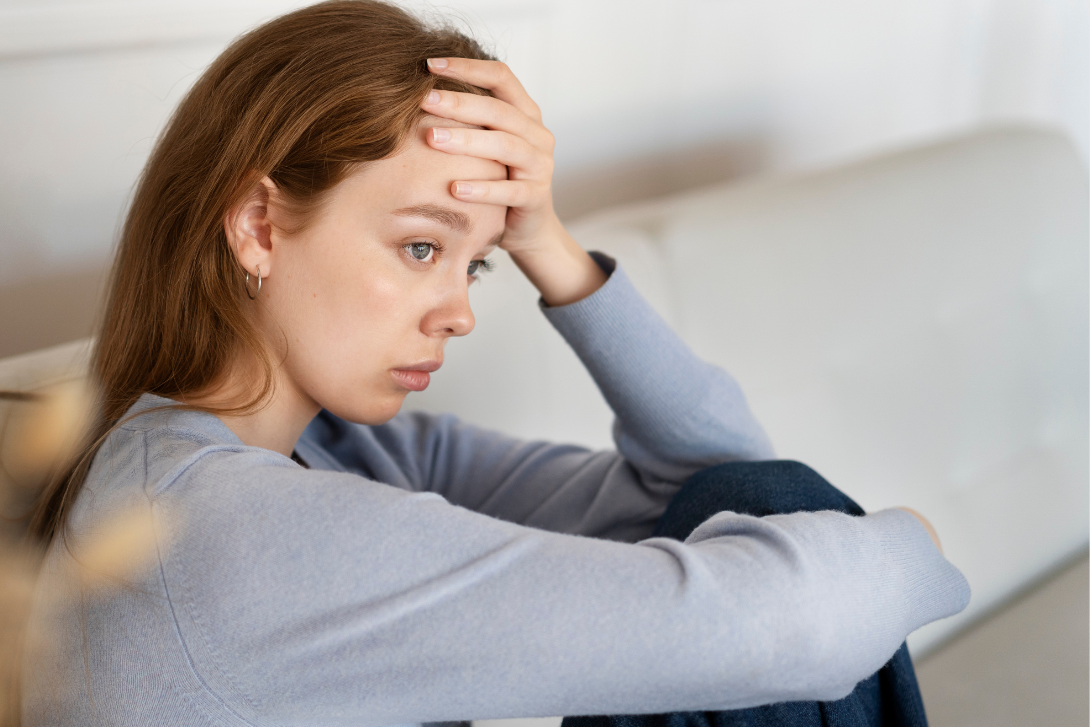 Unhappy lady sitting on a couch with her hand on her forehead